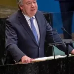 UN Secretary-General António Guterres speaking at a podium next to the United Nations flag during a climate change summit.