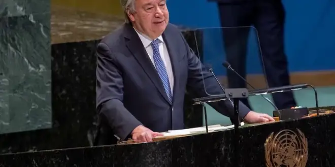 UN Secretary-General António Guterres speaking at a podium next to the United Nations flag during a climate change summit.