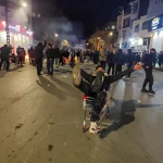 Large crowd of protesters marching on a Tehran street with Iranian flags and banners.