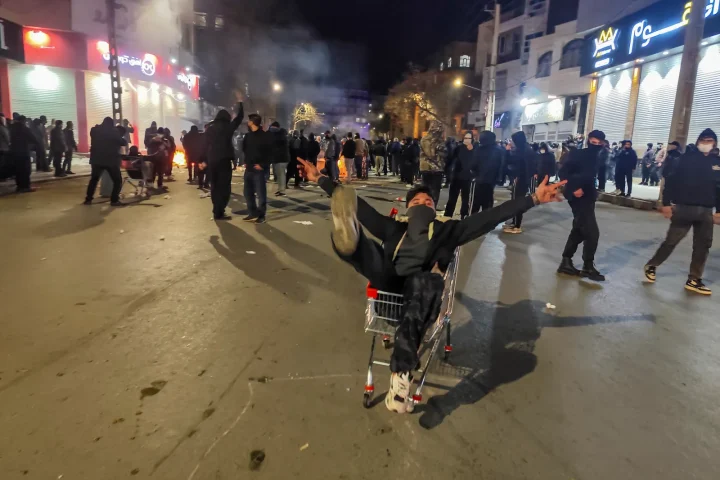 Large crowd of protesters marching on a Tehran street with Iranian flags and banners.